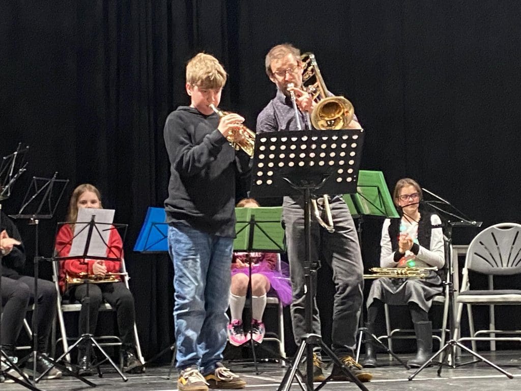 Teacher and student stand at front of training wind band playing a duet on stage