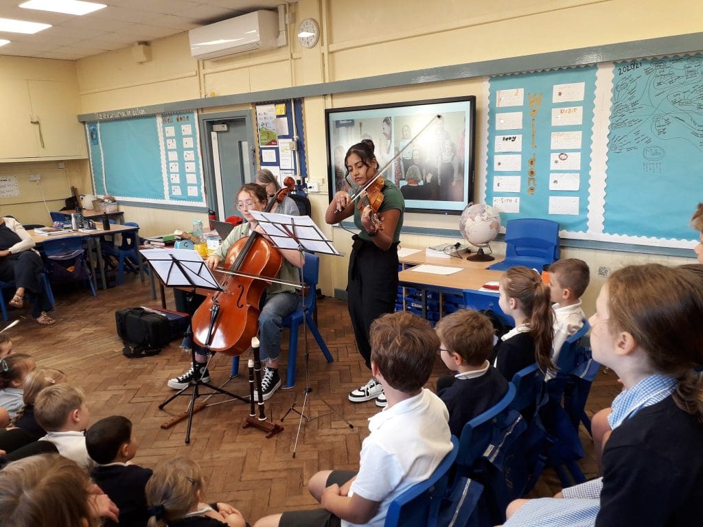 two young people play the cello and violin for a group of school children
