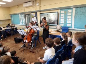 two young people play the cello and violin for a group of school children