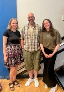 Two music students stand either side of their teacher